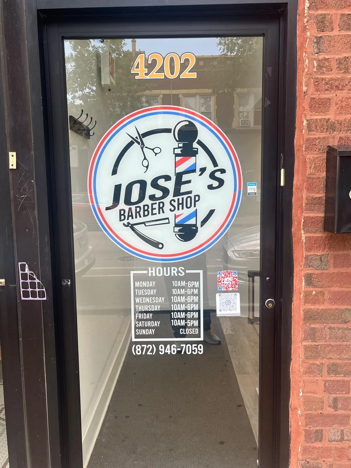 The front door of Jose's Barber Shop at 4202 N Milwaukee Ave, Chicago, showing the logo decal, the posted hours, the phone number and the Instagram QR code