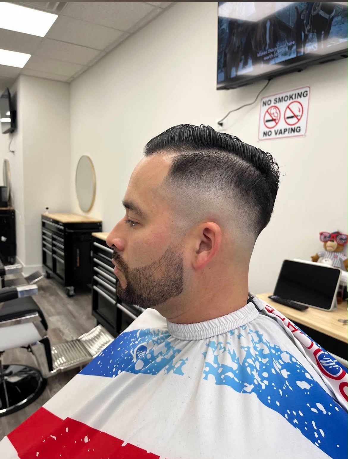 Un skin fade alto con raya marcada a navaja y el cabello peinado de lado arriba, rematado con una barba recortada y delineada — un cliente de perfil en Jose's Barber Shop