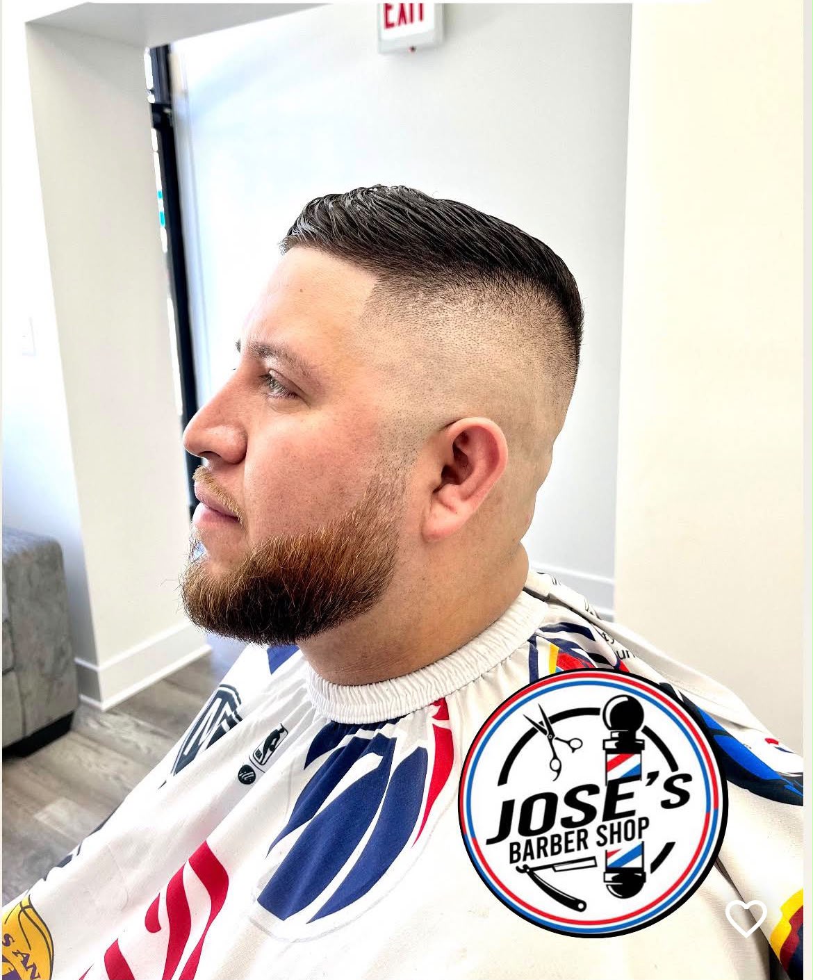 Un corte corto peinado de lado sobre un skin fade alto con raya a navaja, junto con una barba completa perfilada y delineada en la mejilla